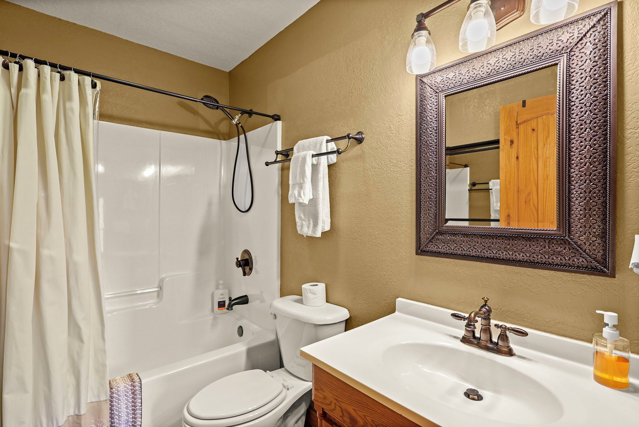 Une salle de bain équipée d’une baignoire, de toilettes, d’un lavabo et d’un miroir avec un cadre décoratif.