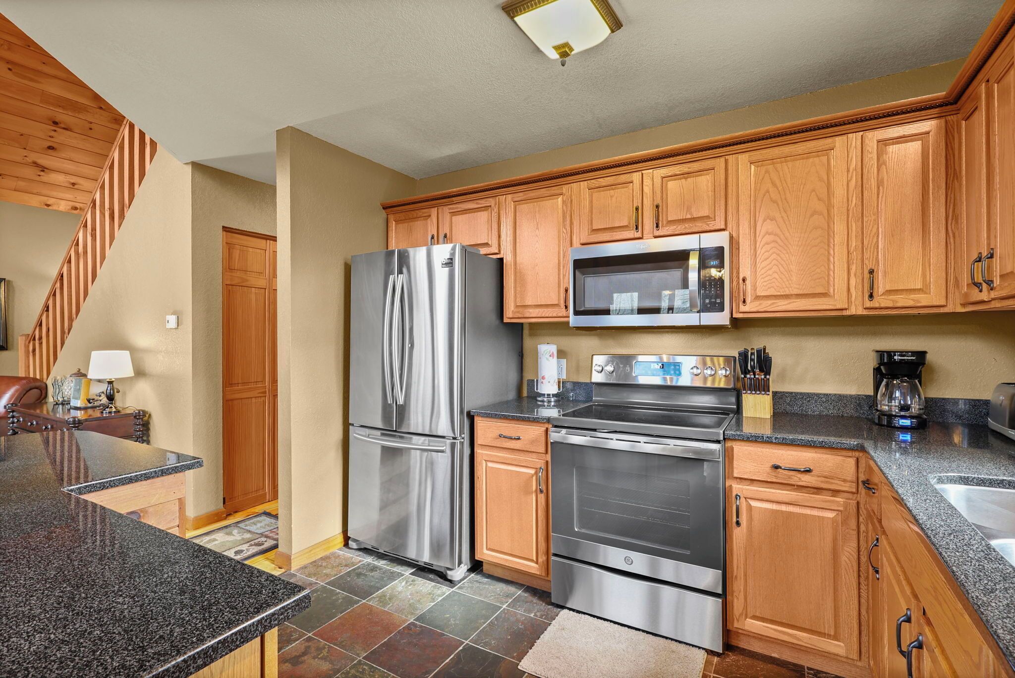 A kitchen with wooden cabinets, stainless steel appliances, granite countertops, and a tiled floor.