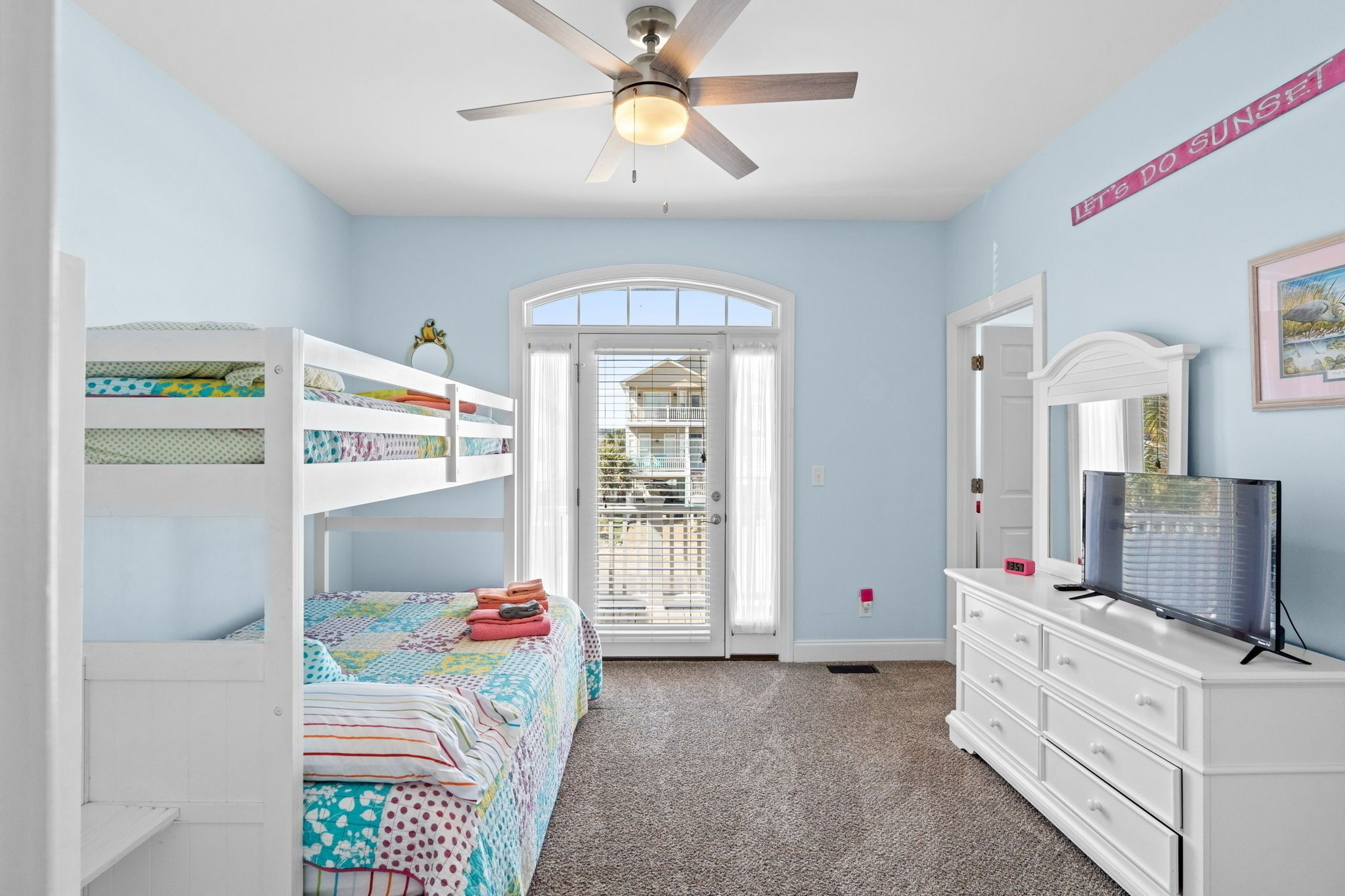 Une chambre avec des lits superposés, une commode, un ventilateur de plafond et une fenêtre avec des stores.