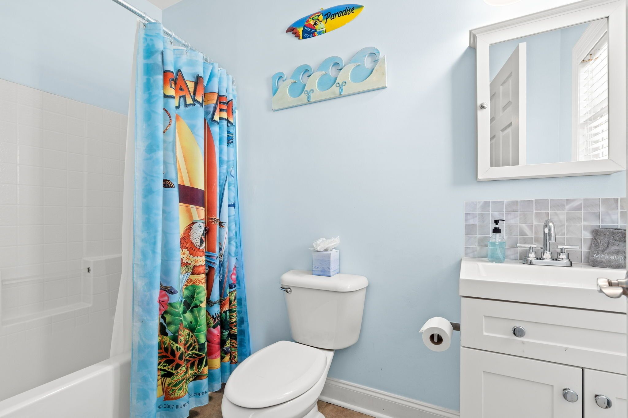 Un bagno con il water bianco, una tenda da doccia con motivo tropicale, un lavandino con specchio e un porta asciugamani.