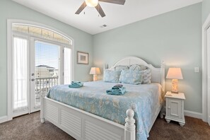 A bedroom with a bed, two bedside lamps, a nightstand, a ceiling fan, and a door with a view of the outside. - Beautiful Oceanfront Family Friendly Home! Linens included 5 bedrooms and 5 bath (Ocean Isle Beach)
