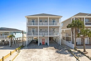 A multi-story beachfront building with balconies, a red door, and a sandy ground area. - Beautiful Oceanfront Family Friendly Home! Linens included 5 bedrooms and 5 bath (Ocean Isle Beach)