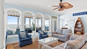 Ein geräumiges Wohnzimmer mit großem Fenster, Deckenventilator und einem Schild mit der Aufschrift 'BEACH HOUSE'.