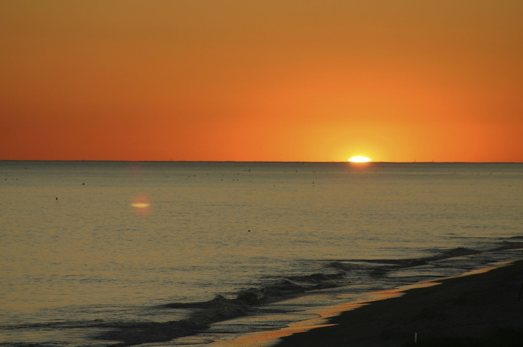 Un coucher de soleil sur une mer calme, avec une plage au premier plan.