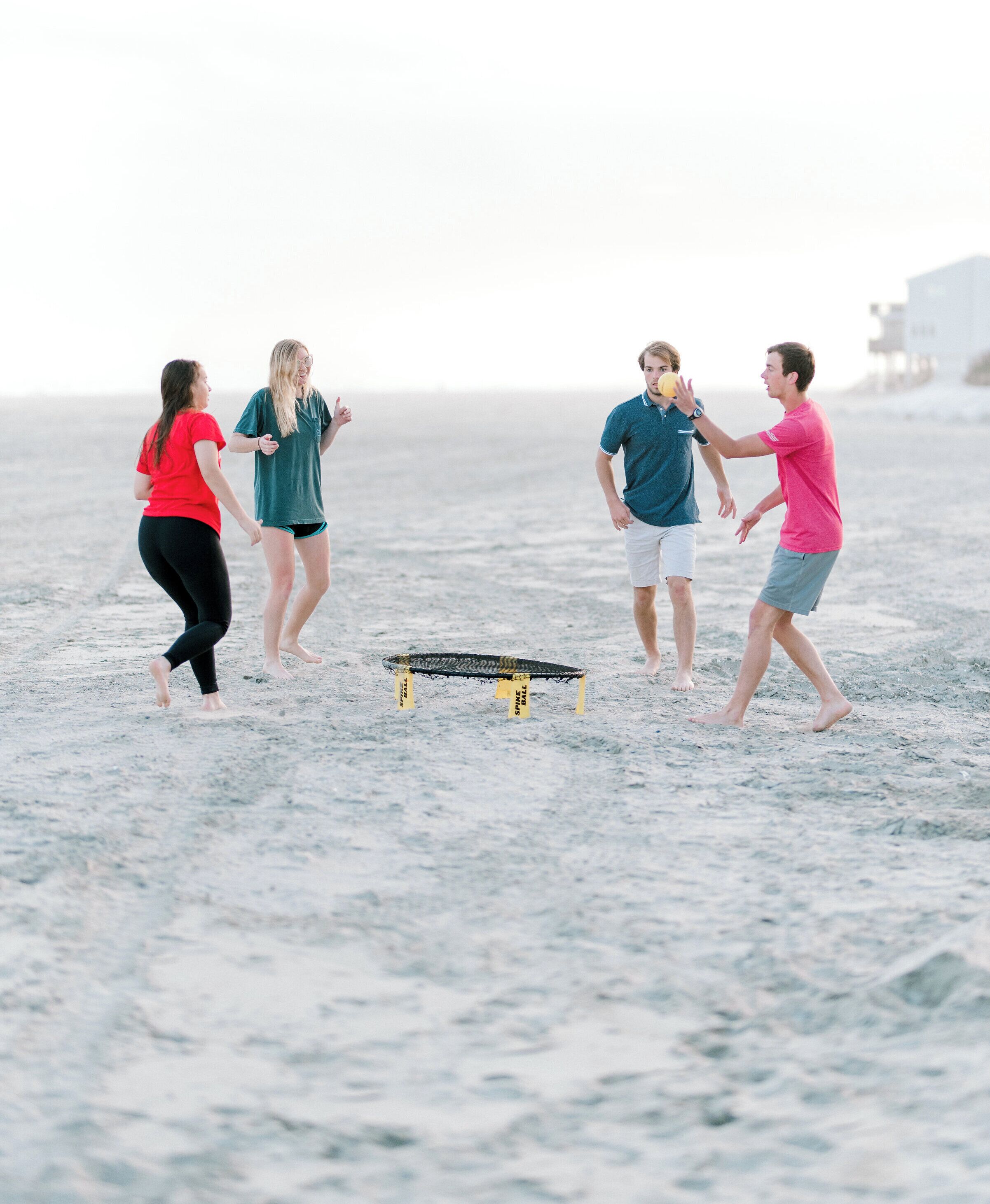 Eine Gruppe Menschen spielt ein Spiel am sandigen Strand, ein kleines Hindernis befindet sich in der Mitte.