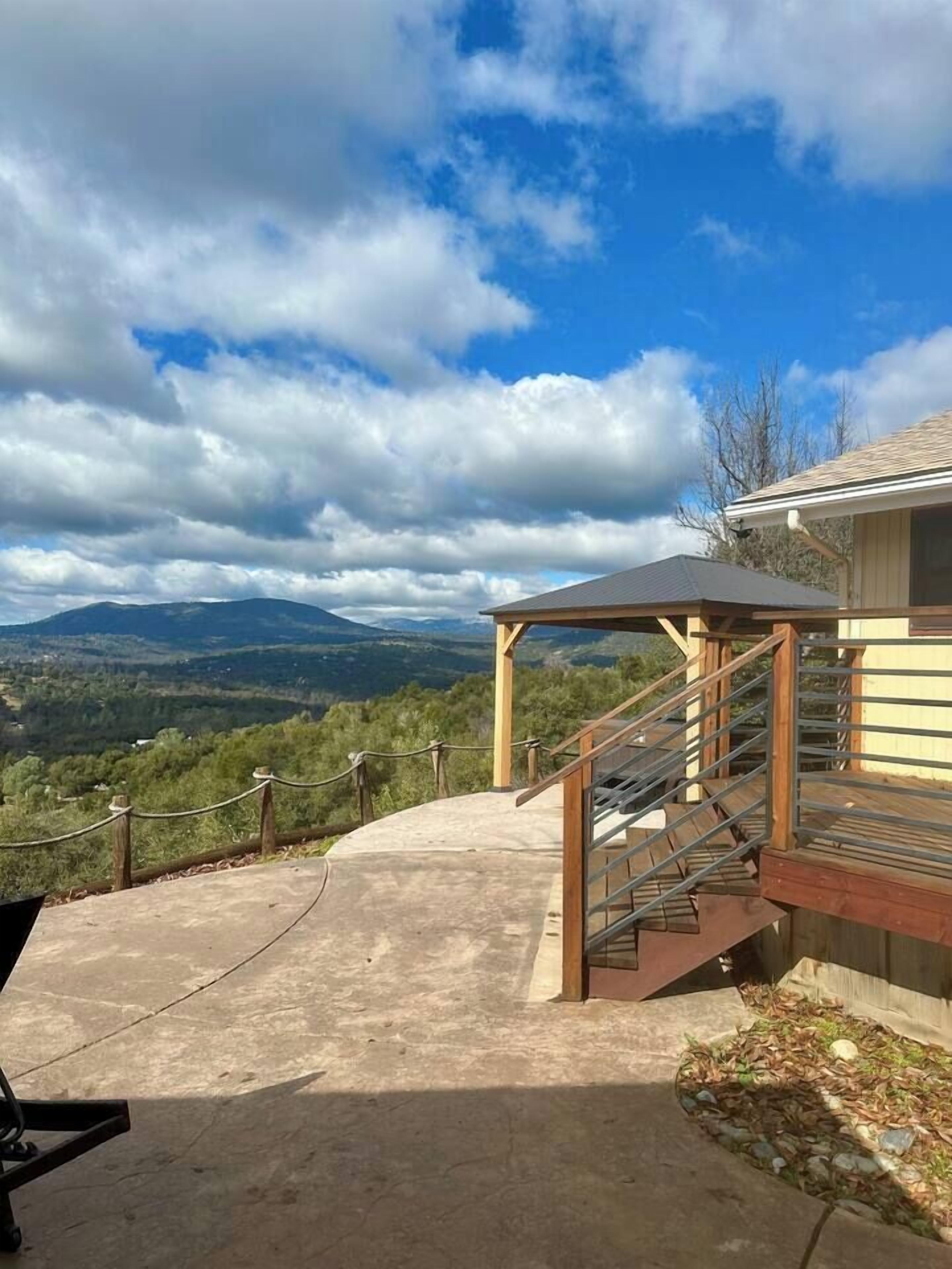 A concrete viewing platform with a wooden staircase leading to a covered area, overlooking a mountainous landscape.