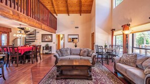 A spacious living area with a wooden ceiling, a dining area with a red tablecloth, and a staircase leading to an upper level.