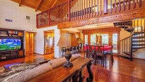 A spacious living area with a wooden ceiling, a dining table set for four, and a staircase leading to an upper level.