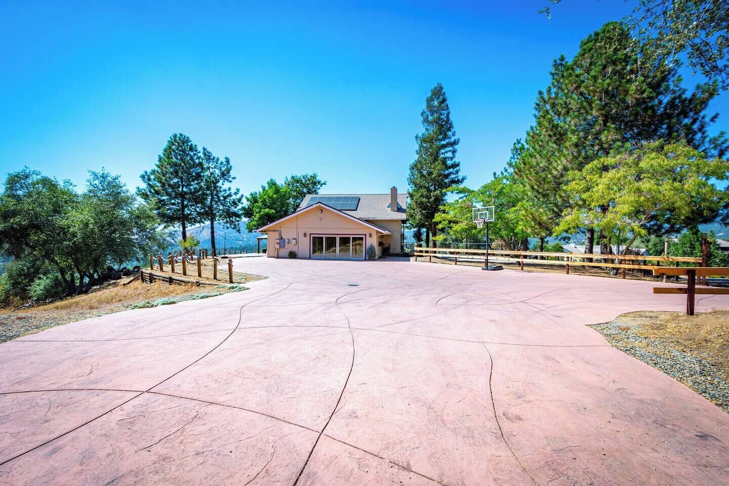A building with a basketball court in front, surrounded by trees and a clear sky.