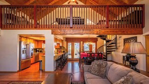 A spacious living area with a high ceiling, wooden staircase, and a kitchen with modern appliances.