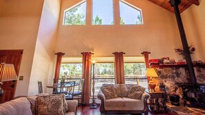 A spacious living room with a high ceiling, large windows, a fireplace, and a stone wall.