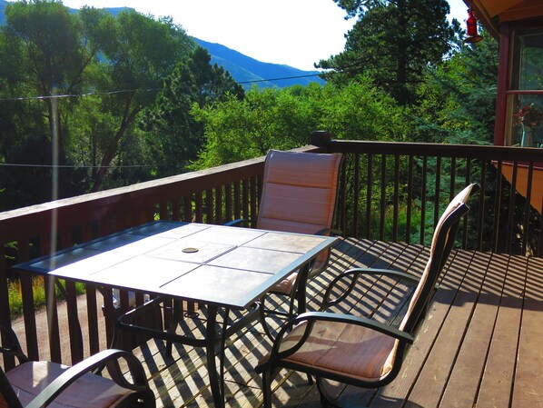An outdoor deck with a table and chairs, surrounded by trees and a mountain view.
