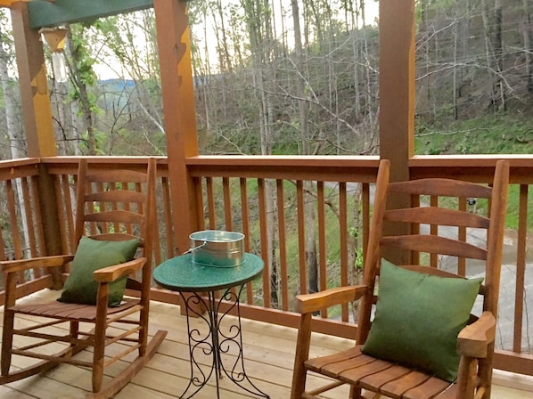 A wooden deck with two chairs and a small table, overlooking a forested area.