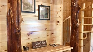 Interior rústico de una cabaña con un escritorio de madera, cuadros enmarcados y un letrero que dice 'The Cabin'.