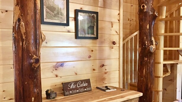 A rustic cabin interior with a wooden desk, framed pictures, and a sign reading "The Cabin." - Now Booking 2027 at THE CURIOUS BEAR ⭐️⭐️⭐️⭐️⭐️ New EV Charger! 2026 on sale (Gatlinburg)