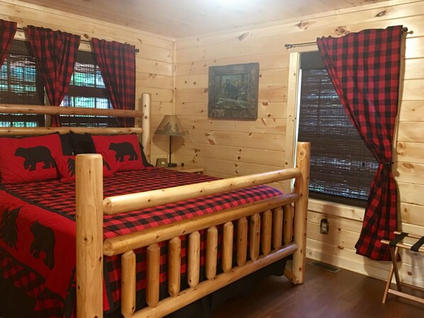 A wooden cabin room with a bed, curtains, a lamp, and a window.