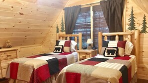 A cozy cabin room with two wooden beds, each with a quilted bedspread and pillows, a small desk, and a window with curtains. - Now Booking 2027 at THE CURIOUS BEAR ⭐️⭐️⭐️⭐️⭐️ New EV Charger! 2026 on sale (Gatlinburg)