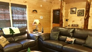 Un interior de cabaña acogedor con dos sofás de cuero, una mesa de centro de madera y una lámpara.