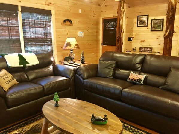 Ein gemütliches Blockhaus-Interieur mit zwei Ledersofas, einem Holztisch und einer Lampe.