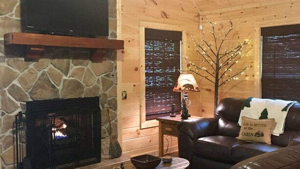 Interior acogedor de una cabaña con chimenea de piedra, sofá de cuero y televisor montado en la pared.