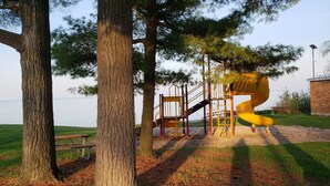 A playground with a yellow spiral slide and a wooden bench near a lake. - The Boathouse Cottage (Fort Gratiot Twp)
