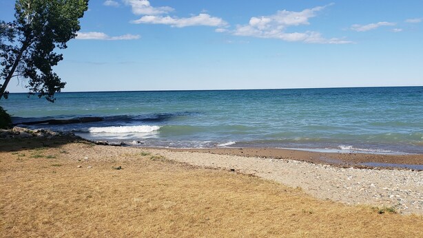 A beach with a wooden fence, pebbles, and a clear sky. - The Boathouse Cottage (Fort Gratiot Twp)