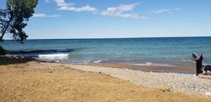 A beach with a wooden fence, pebbles, and a clear sky. - The Boathouse Cottage (Fort Gratiot Twp)