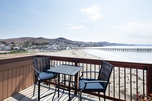En terrass med två stolar och ett bord med utsikt över en strand, en brygga och avlägsna kullar.