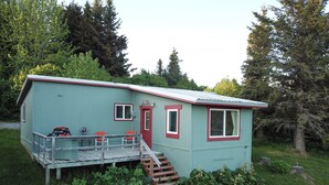 Ein kleines, eingeschossiges Haus mit Veranda und roter Tür, umgeben von viel Grün.