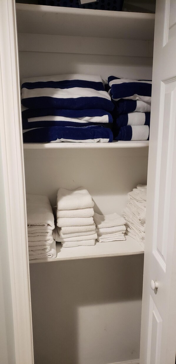 A closet with shelves holding folded towels in blue and white, and a white door. - The Lighthouse Cottage - Sleeps 8 (Fort Gratiot Twp)
