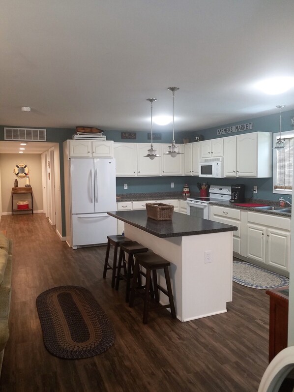 A modern kitchen with white cabinets, a central island with stools, and a sign reading "Farmers Market".