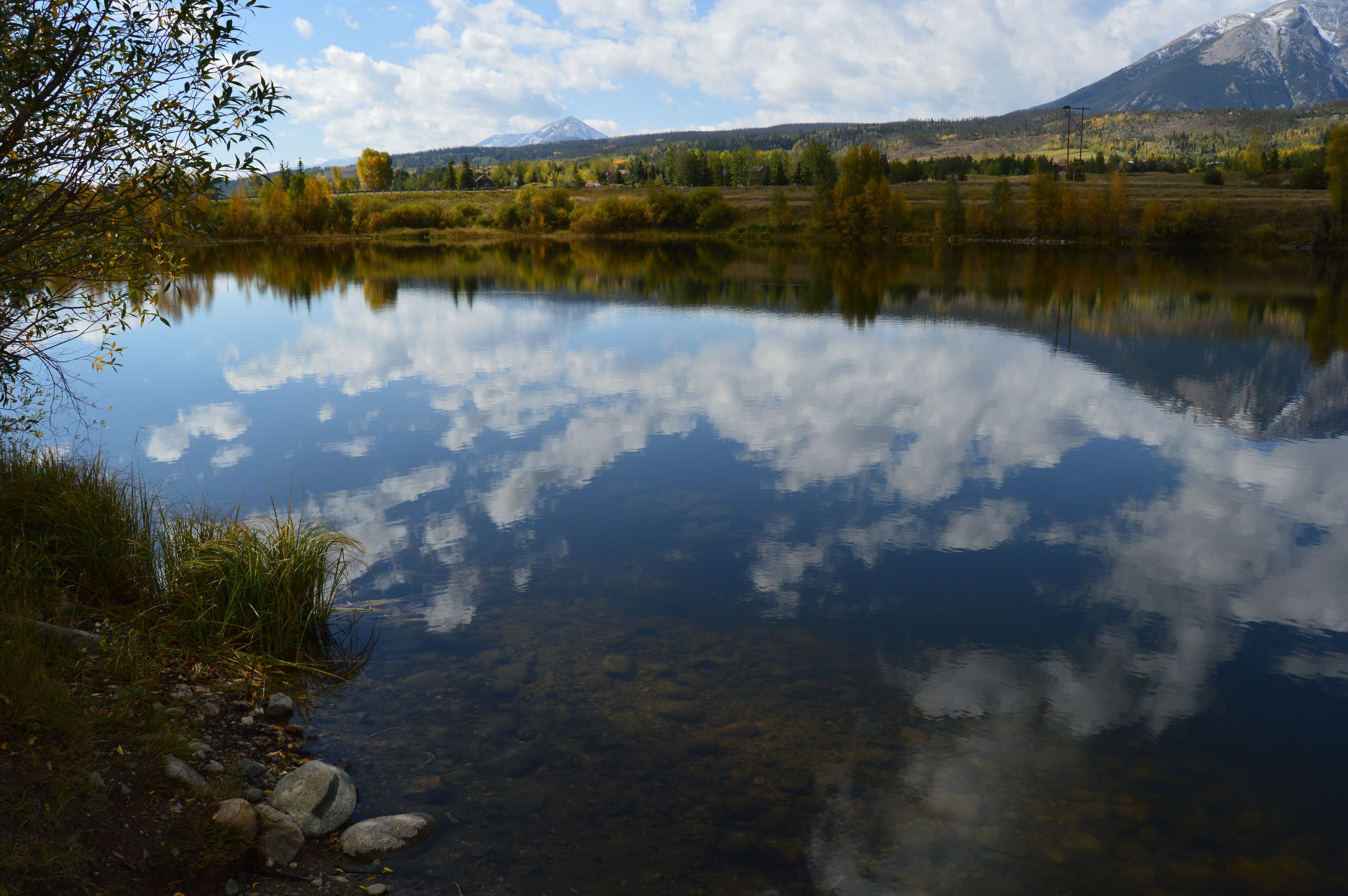 A calm lake with clear reflections of trees and a mountain in the background.