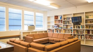 Una biblioteca con un sofá modular, estanterías, un televisor y ventanas amplias.