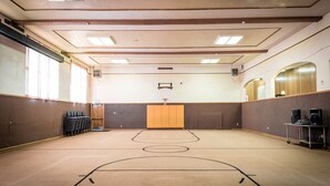 Una amplia cancha de baloncesto cubierta con suelo de madera, un aro de baloncesto y una zona de estar con sillas.