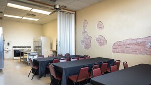 Un salón de conferencias con una larga mesa, sillas rojas, una pizarra y una zona de cocina.