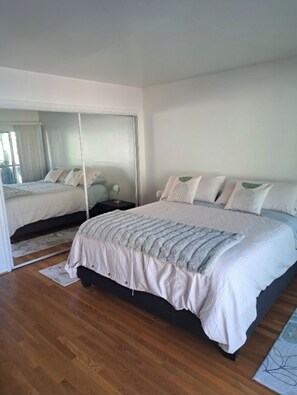 A bedroom with a large bed, a nightstand, a mirror, and a wooden floor. - Beachy Private Get-A-Way!! Large Deck facing Ocean! (Playa Del Rey)