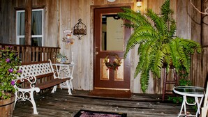 A wooden porch with a bench, a small table, and a potted plant. - The Shebeen A small Irish cottage,come experience the enchantment and trnquility (Brooksville)
