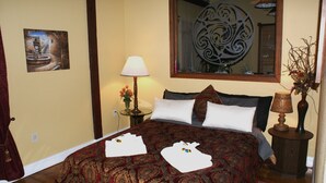 A hotel room with a bed, a nightstand, a lamp, a vase with flowers, a painting on the wall, and a mirror. - The Shebeen A small Irish cottage,come experience the enchantment and trnquility (Brooksville)