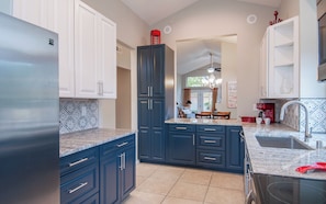 A modern kitchen with dark blue cabinets, a granite countertop, and a stainless steel refrigerator.