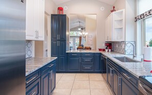 A kitchen with dark blue cabinets, a granite countertop, and a view into the dining area.