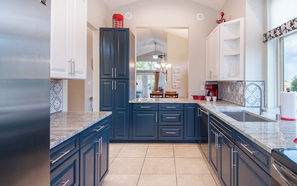 A kitchen with dark blue cabinets, a granite countertop, and a view into the dining area. - Quiet Convenient Comfort in Gated Community (Albuquerque)