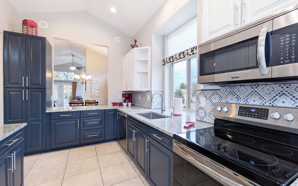 A modern kitchen with dark cabinetry, a large island, stainless steel appliances, and a view to the outdoors.