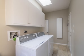A laundry room with a front-loading washer and dryer, a white cabinet above, and a door leading to another room.