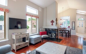 A living room with a flat-screen TV, a fireplace, a dining area with a chandelier, and a view of the outside. - Quiet Convenient Comfort in Gated Community (Albuquerque)