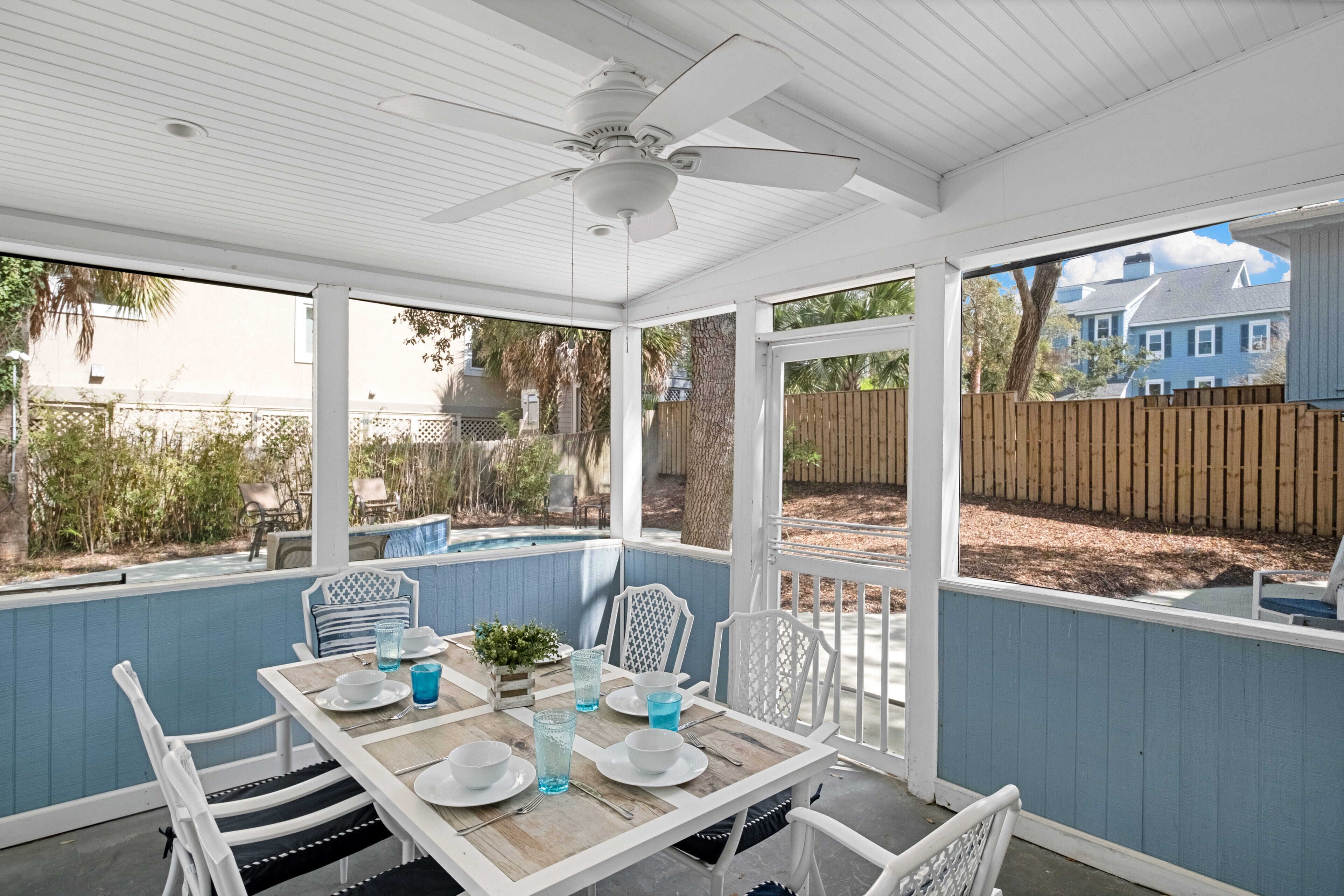 Eine überdachte Terrasse mit Esstisch, weißen Stühlen und Deckenventilator.