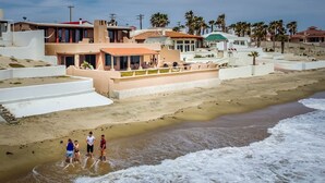 Una propiedad frente a la playa con una arena dorada, algunas personas cerca del agua y casas de estilo arquitectónico moderno.