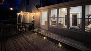 Eine Holzdielen-Terrasse mit Lichterkette, einem überdachten Sitzbereich und Blick ins Haus durch große Fenster.