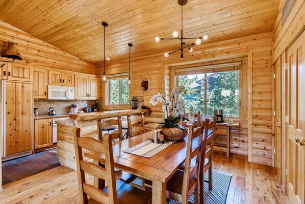 A wooden cabin interior with a kitchen, dining area, and large windows.