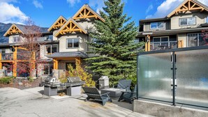 A residential building with a stone facade, wooden accents, and a patio with outdoor furniture. - Copperstone 2BR in the Canadian Rockies - Dog-Friendly, Shared Hot Tub (Dead Man's Flats)