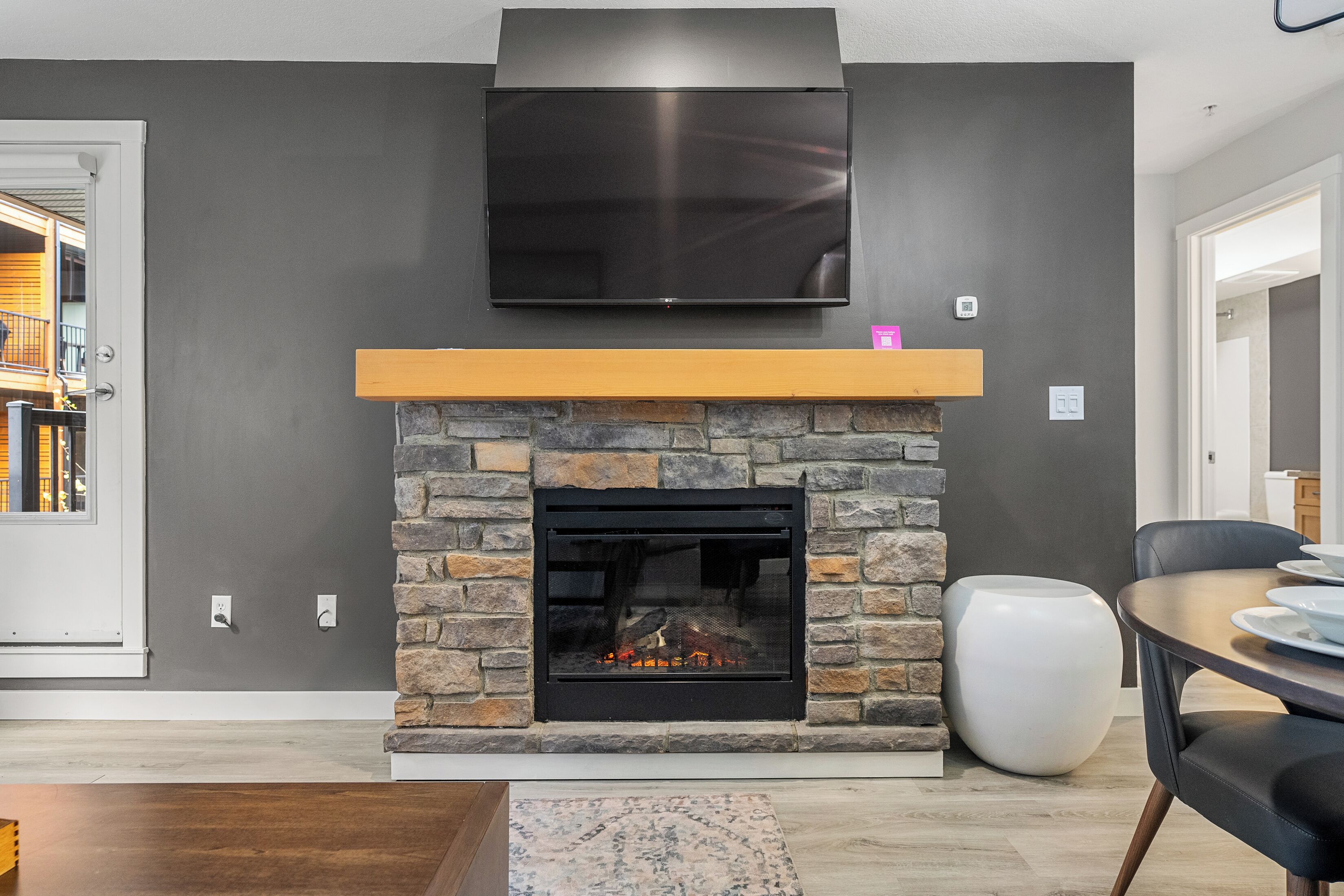 A modern living room with a stone fireplace, a mounted flat-screen TV, and a dining area with a round table and chairs.